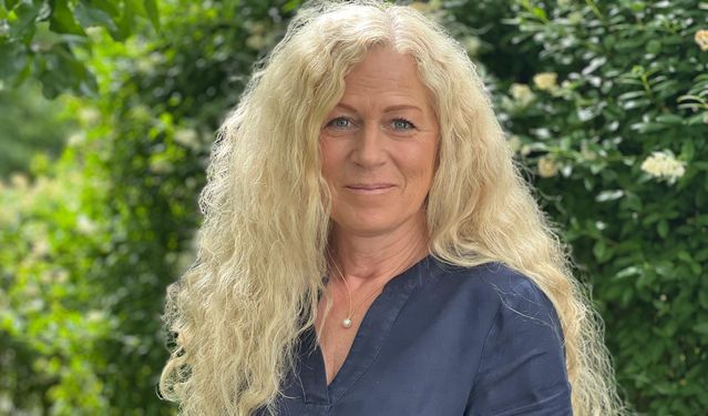 Porträt von M.Sc. Psych. Katrin Bonato-Ehrenthal in einer dunkelblauen Bluse vor einem grünen, blühenden Hintergrund.