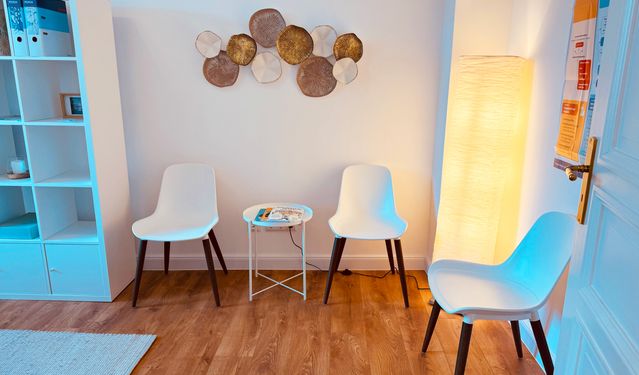 Freundlich eingerichteter Praxisraum mit grünem Sofa, hellem Sessel, Holztisch und Zimmerpflanzen.